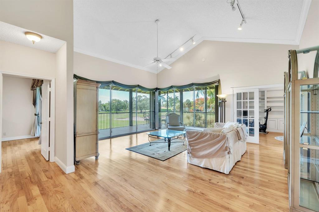 A living room with hardwood floors, vaulted ceilings, and large glass doors overlooking a golf course — 7644 Elmridge Drive, Boca Raton FL 33433, BOCA RATON, FL