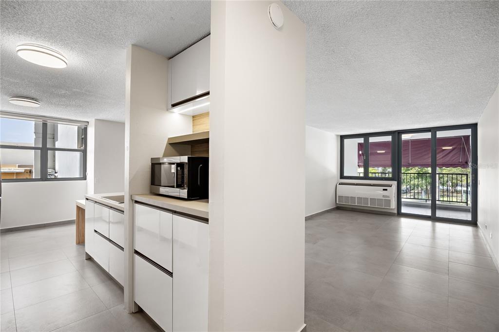 A modern kitchen with white cabinets and a microwave opens into a spacious living area — 253 CHILE UNIT 1-C, SAN JUAN, PR