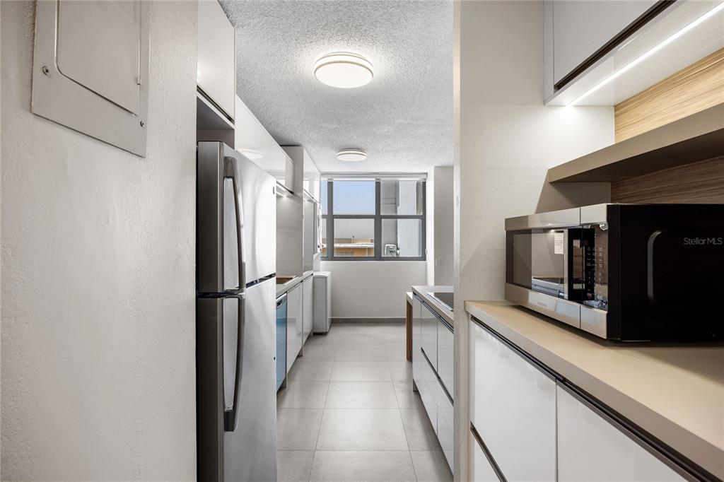 A galley-style kitchen features stainless steel appliances, white cabinetry, and light-colored tile flooring — 253 CHILE UNIT 1-C, SAN JUAN, PR