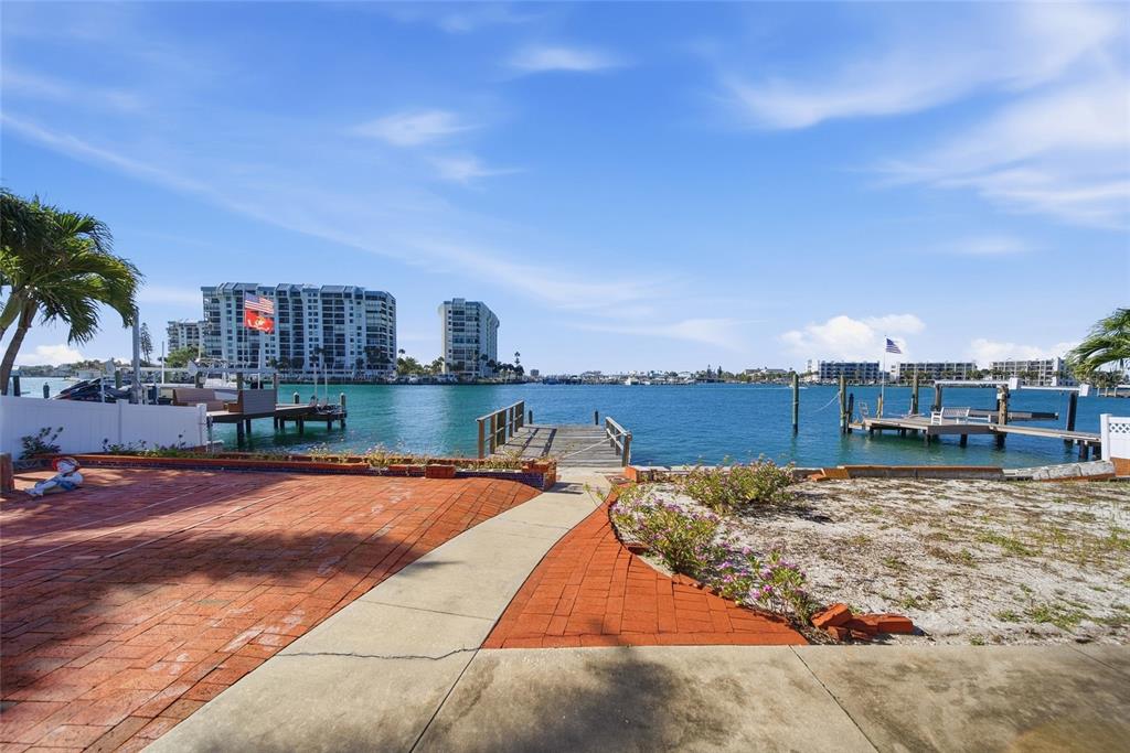A brick patio leads to a wooden dock overlooking a wide bay with distant buildings — 4 BELLEVUE DRIVE, TREASURE ISLAND, FL