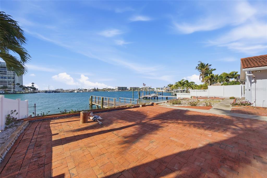 A brick patio overlooks a waterfront view with a wooden dock and distant buildings — 4 BELLEVUE DRIVE, TREASURE ISLAND, FL