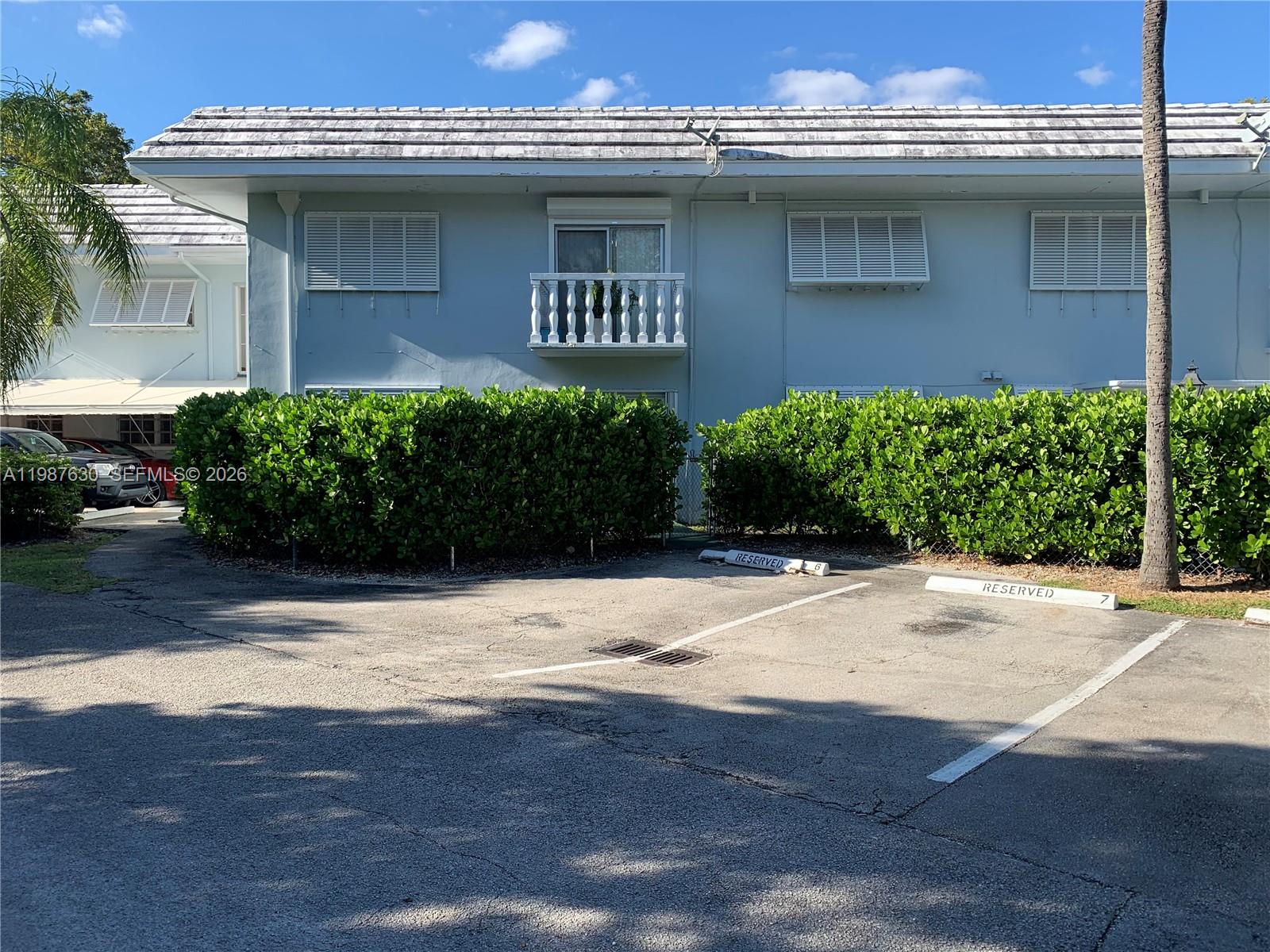 A two-story light blue building features a small balcony and reserved parking spaces in front — 1200 Mariposa Ave # E104, Coral Gables FL 33146, CORAL GABLES, FL