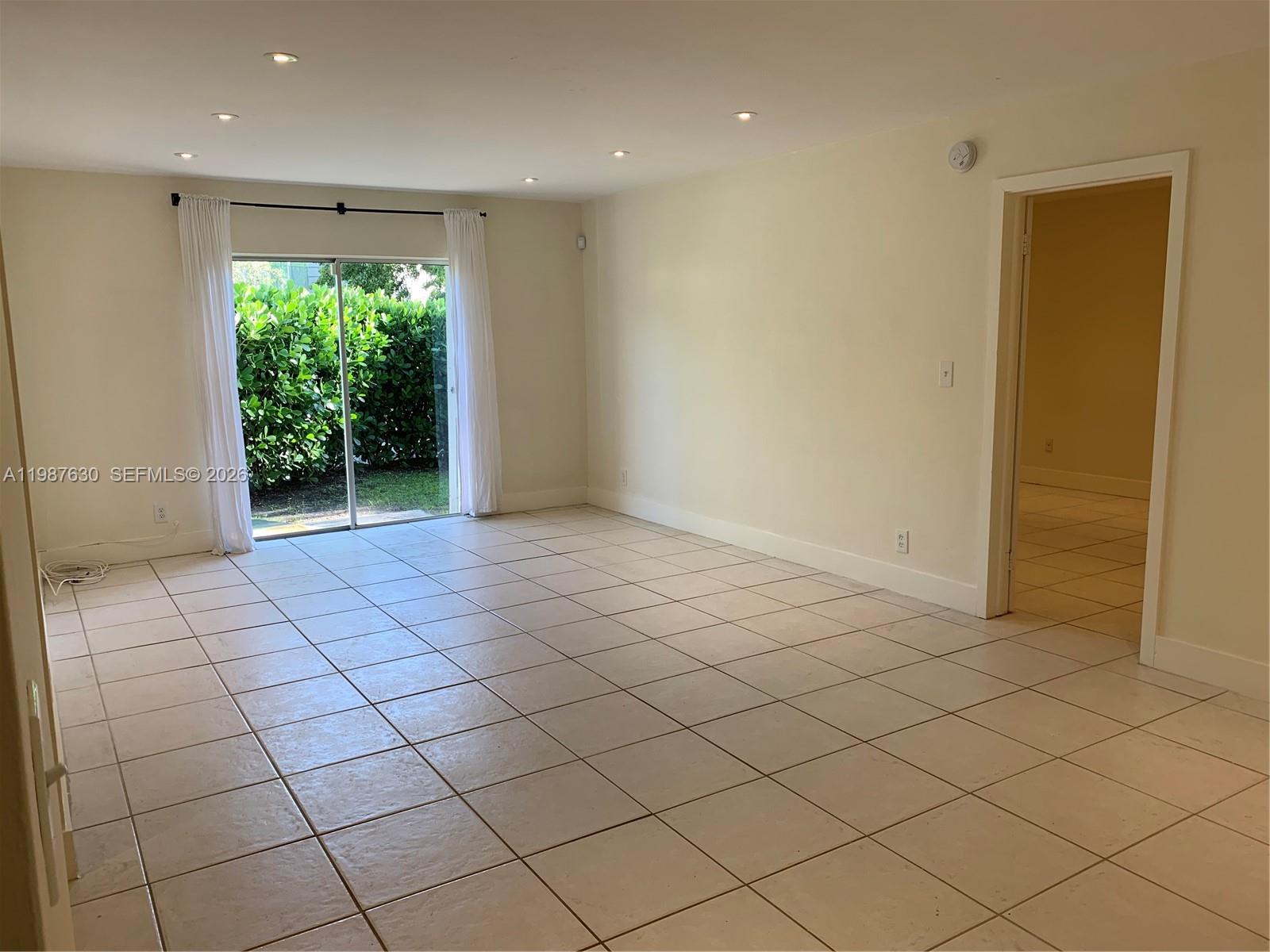 An empty room with beige tile flooring, recessed lighting, and a sliding glass door — 1200 Mariposa Ave # E104, Coral Gables FL 33146, CORAL GABLES, FL