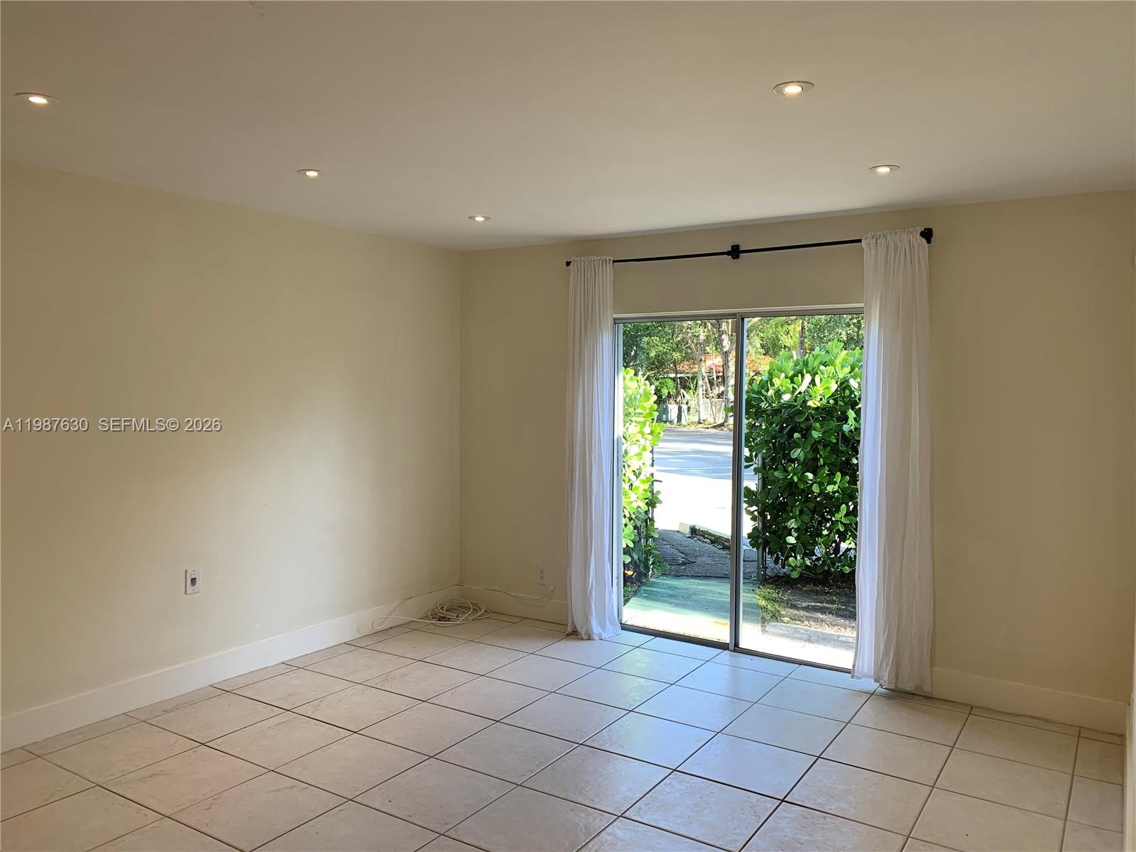 An empty room features beige walls, light-colored tile flooring, recessed lighting, and a sliding glass door — 1200 Mariposa Ave # E104, Coral Gables FL 33146, CORAL GABLES, FL