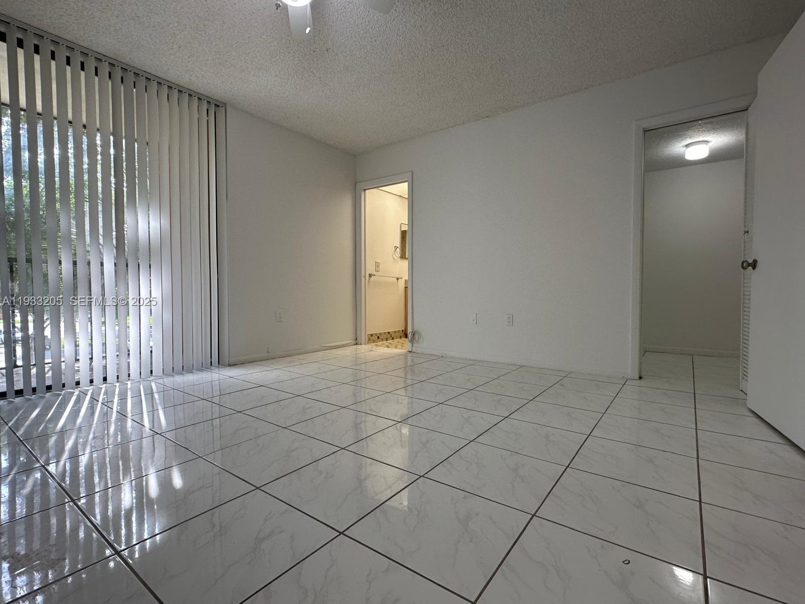 An empty room features white tiled floors, a popcorn ceiling, and vertical blinds — 8420 SW 133rd Ave Rd # 317, Miami FL 33183, MIAMI, FL