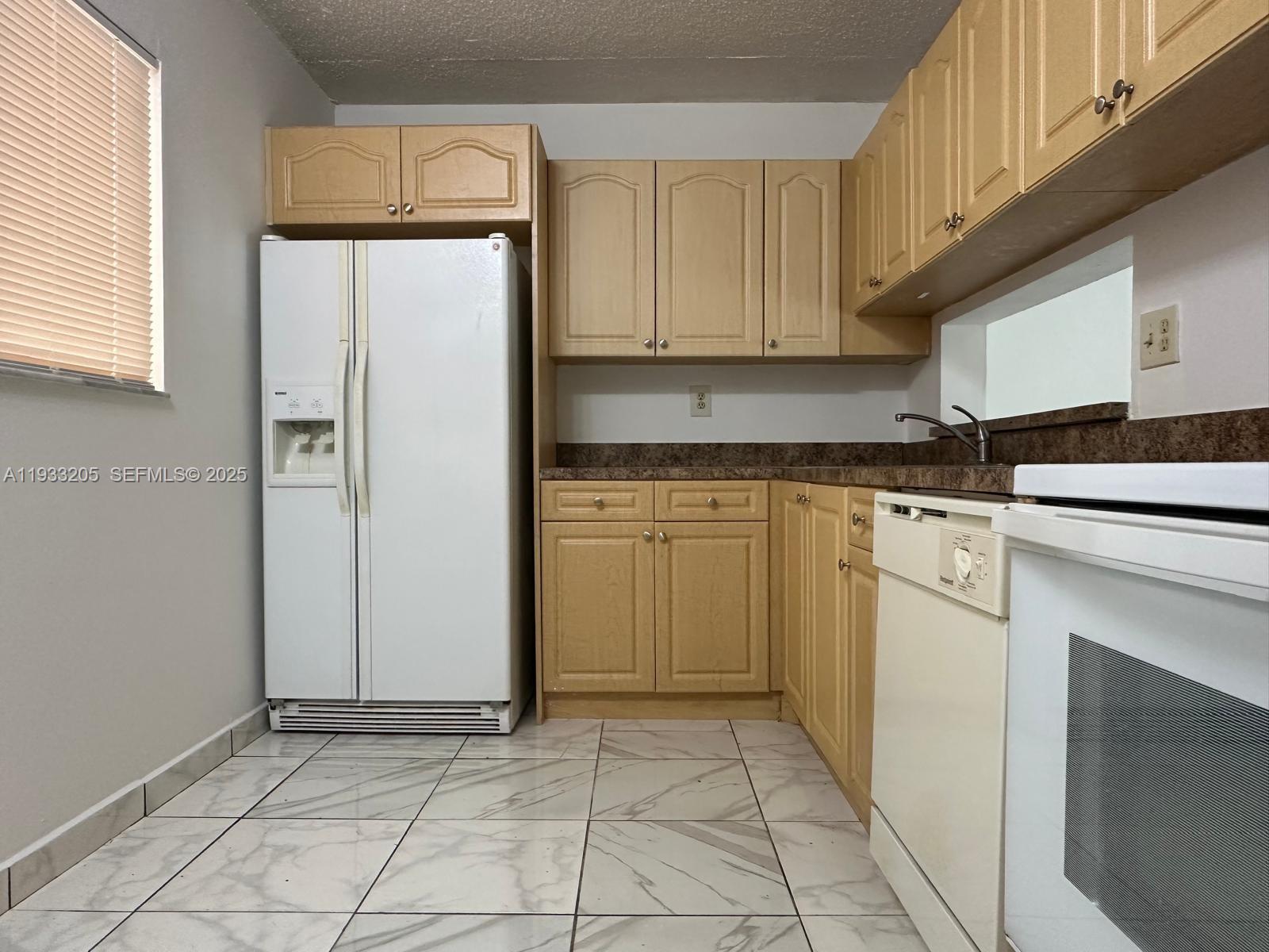 A kitchen features light wood cabinets, white appliances, dark countertops, and white marble-patterned tile flooring — 8420 SW 133rd Ave Rd # 317, Miami FL 33183, MIAMI, FL