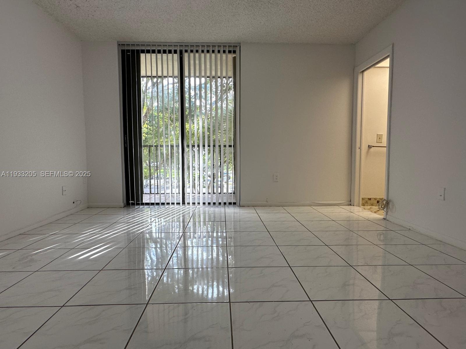 An empty room features white tiled floors, a popcorn ceiling, and a sliding glass door — 8420 SW 133rd Ave Rd # 317, Miami FL 33183, MIAMI, FL