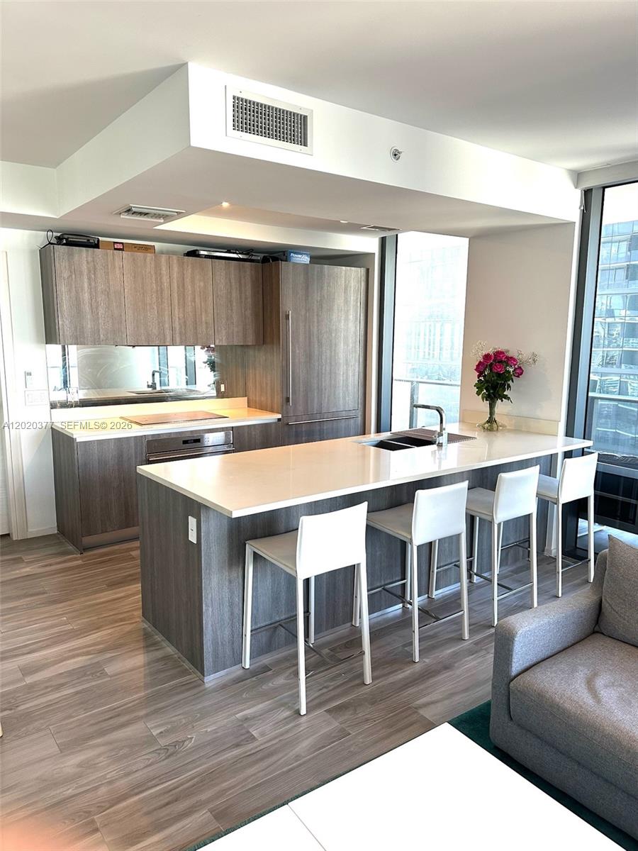 A modern kitchen features wood-grain cabinetry, a white quartz island, and four white bar stools — 801 S Miami Ave # 4305, Miami FL 33130, MIAMI, FL
