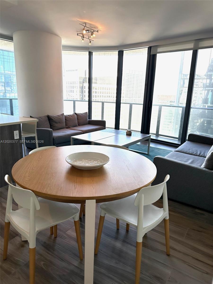 A dining area with a round wooden table sits before a living room with floor-to-ceiling windows — 801 S Miami Ave # 4305, Miami FL 33130, MIAMI, FL