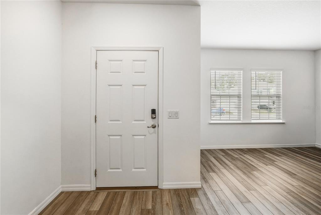 An interior view of an entryway featuring a white door, light walls, and wood flooring — 670 NW 243RD TERRACE, NEWBERRY, FL