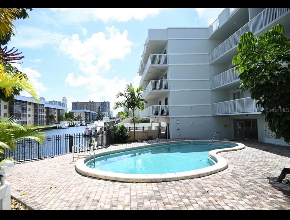 A kidney-shaped swimming pool sits on a brick patio beside a multi-story apartment building — 3527 NE 168TH STREET UNIT 208, NORTH MIAMI BEACH, FL