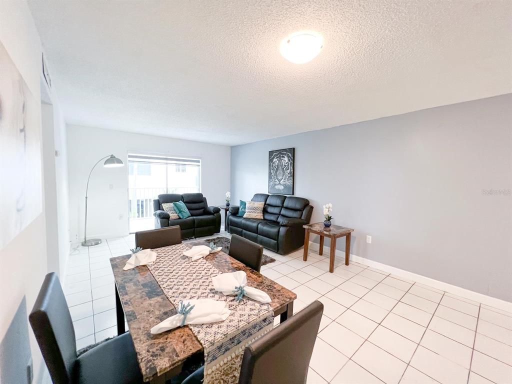 A dining area with a marble-topped table flows into a living room with black furniture — 3527 NE 168TH STREET UNIT 208, NORTH MIAMI BEACH, FL