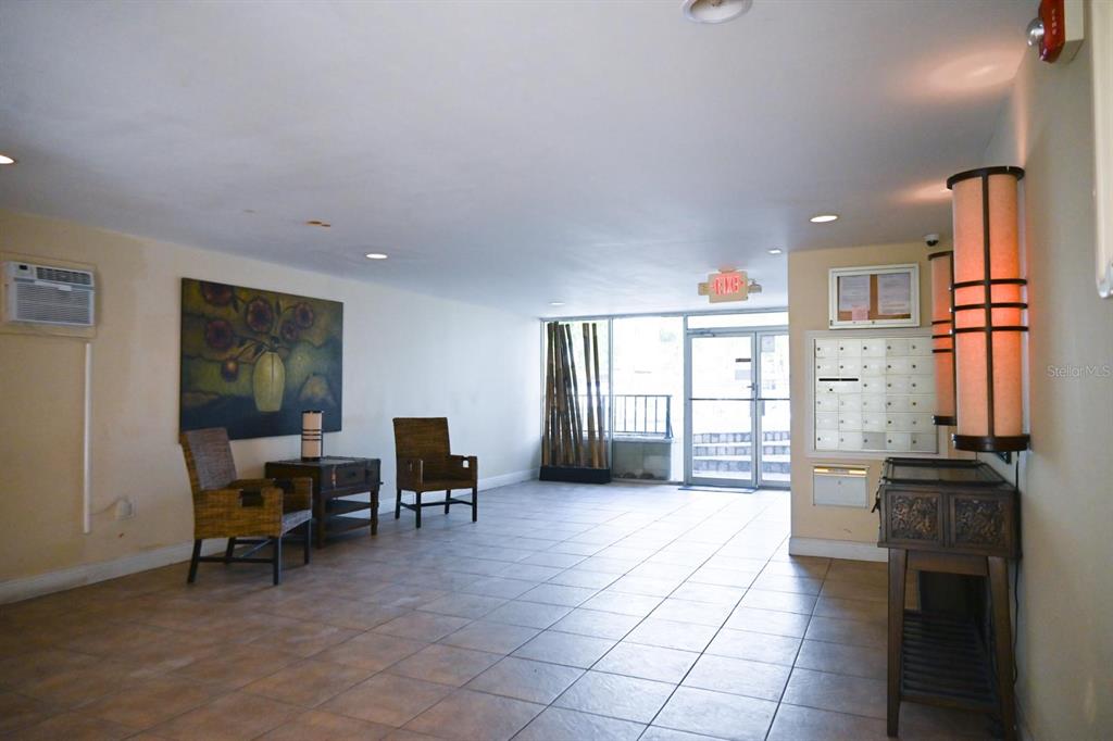 A lobby area features tile flooring, wicker chairs, a wall painting, and a mail station — 3527 NE 168TH STREET UNIT 208, NORTH MIAMI BEACH, FL