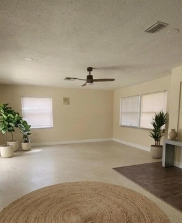 A spacious, light-filled living room features beige walls, tile flooring, and a ceiling fan — 2421 ARCHER BOULEVARD, ORLANDO, FL