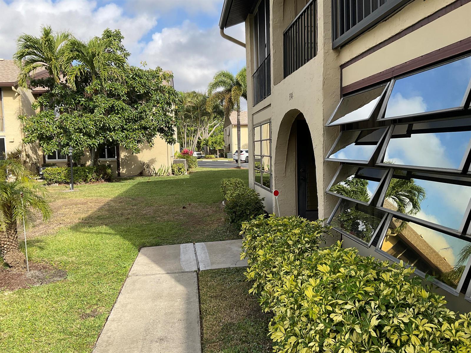 A view of a tan apartment building exterior with a walkway and landscaped lawn — 334 Pine Ridge Circle # 1, FL 33463, FL