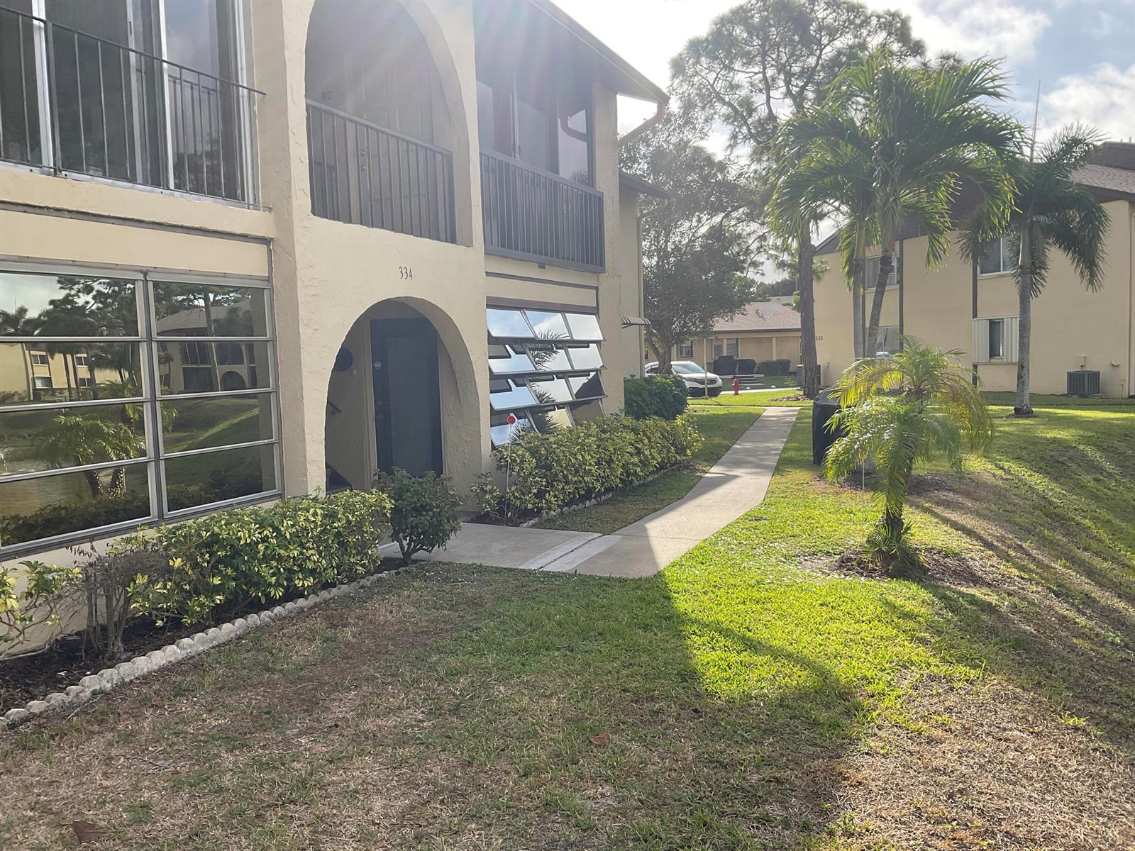A two-story apartment building with arched entryways, louvered windows, and a landscaped walkway — 334 Pine Ridge Circle # 1, FL 33463, FL