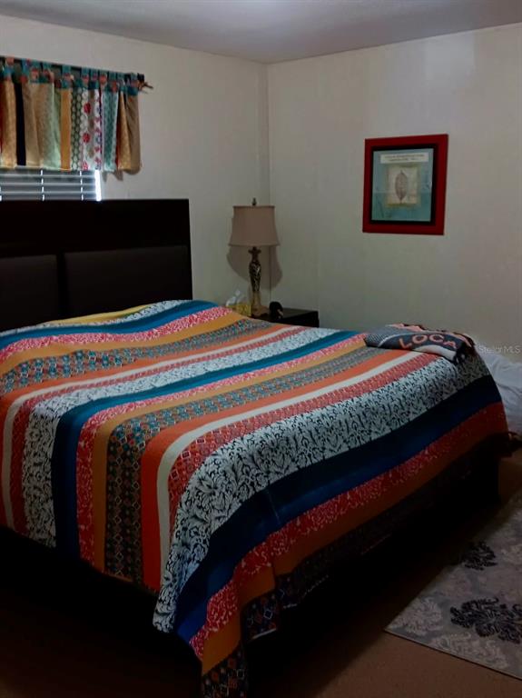 A bedroom features a bed with a colorful striped quilt, a lamp, and wall art — 17749 SE 156TH PLACE ROAD, WEIRSDALE, FL