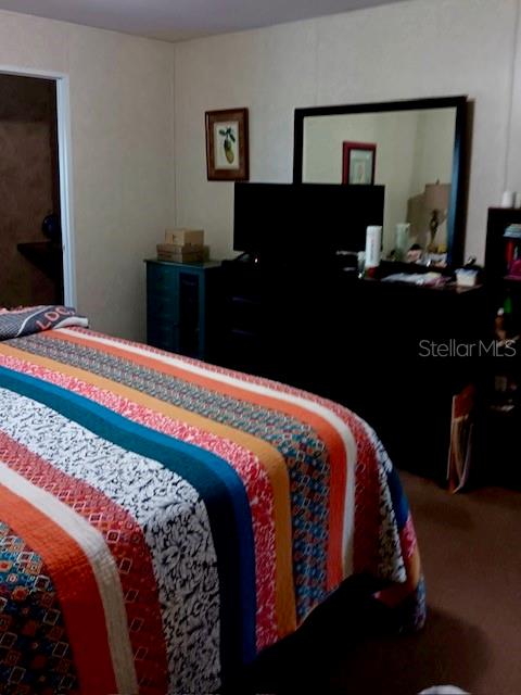 A bedroom features a bed with a colorful striped quilt and a dark wood dresser — 17749 SE 156TH PLACE ROAD, WEIRSDALE, FL