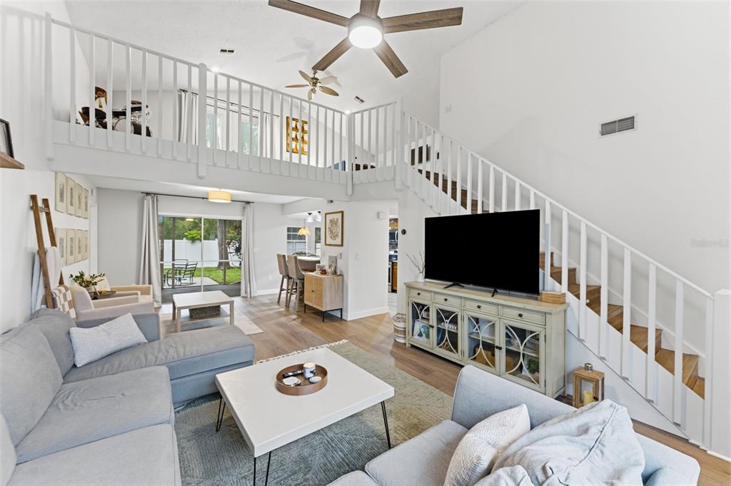 A living room with a loft, white railings, a television, and a sliding glass door — 7226 HUMMINGBIRD LANE, NEW PORT RICHEY, FL