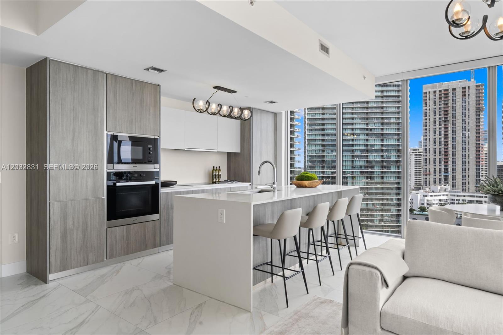 A modern kitchen features gray wood cabinetry, a white island with bar seating, and floor-to-ceiling windows — 2900 NE 7th Ave # 1902, Miami FL 33137, MIAMI, FL