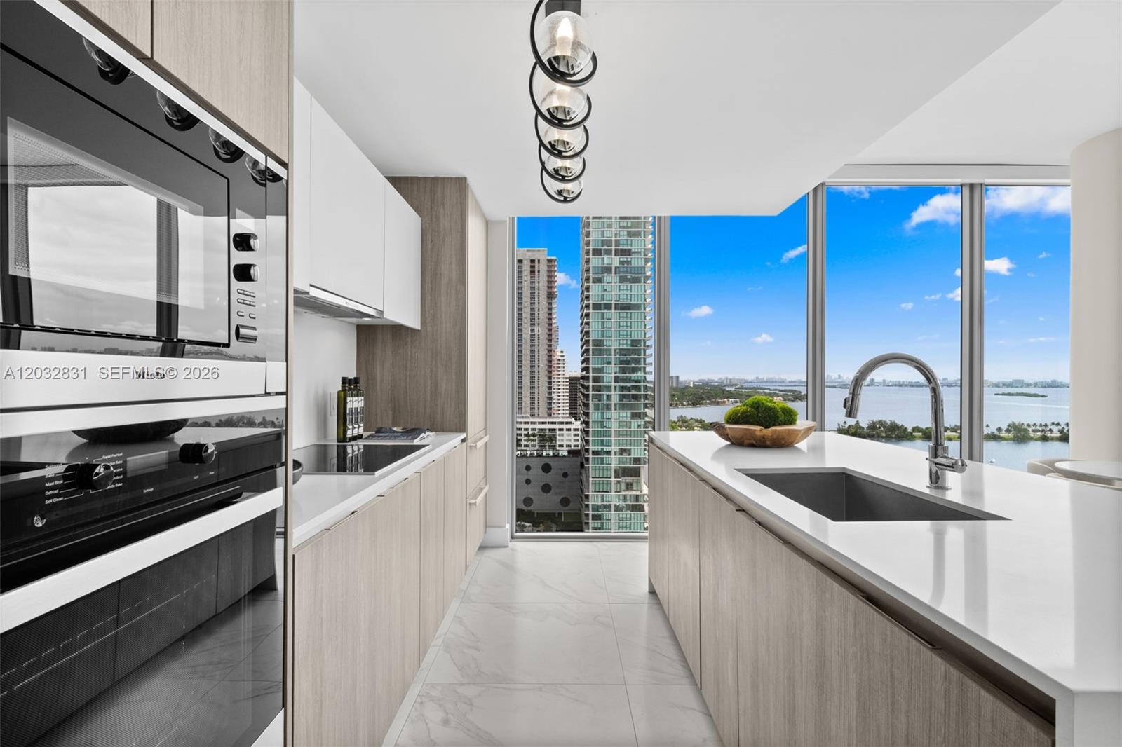 A modern kitchen features light wood cabinetry, white countertops, and floor-to-ceiling windows overlooking the city — 2900 NE 7th Ave # 1902, Miami FL 33137, MIAMI, FL