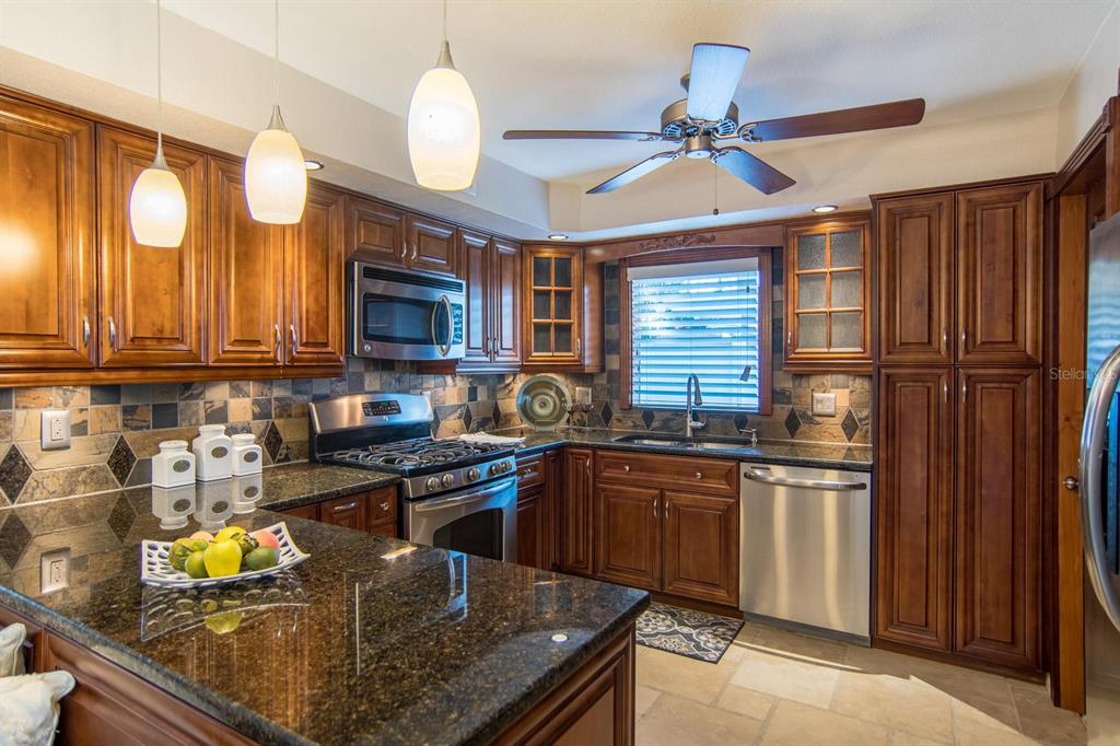 A kitchen with dark wood cabinets, granite countertops, stainless steel appliances, and a ceiling fan — 542 59TH WAY S, ST PETERSBURG, FL