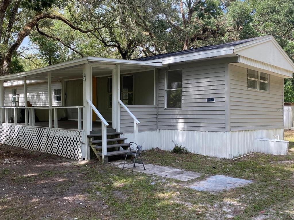 A single-story mobile home with gray horizontal siding, a covered front porch, and lattice skirting — 19429 MCCLOY CIRCLE, BROOKSVILLE, FL