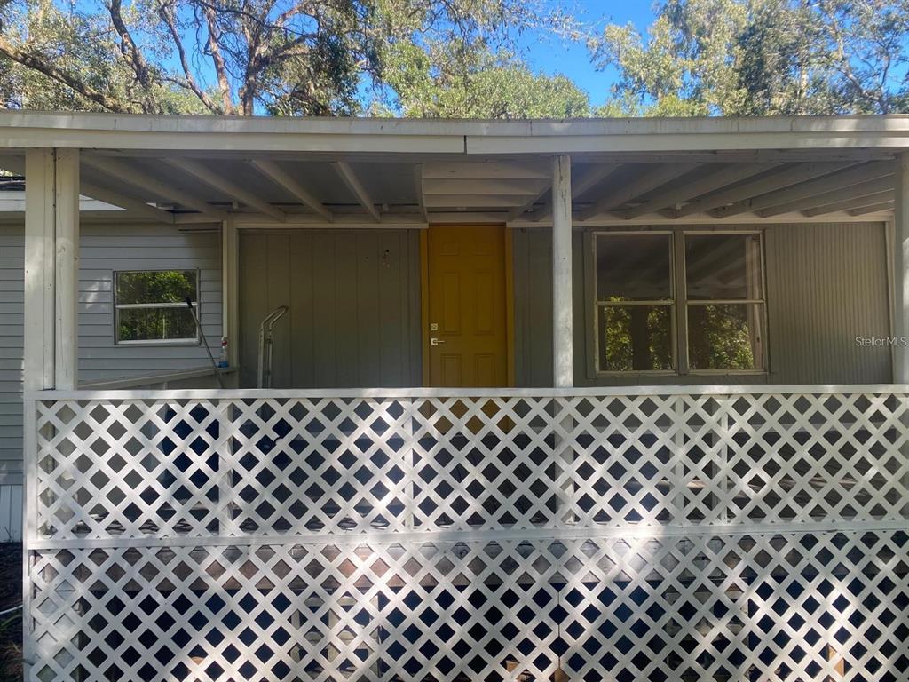 A covered porch with white lattice railing leads to a yellow front door — 19429 MCCLOY CIRCLE, BROOKSVILLE, FL