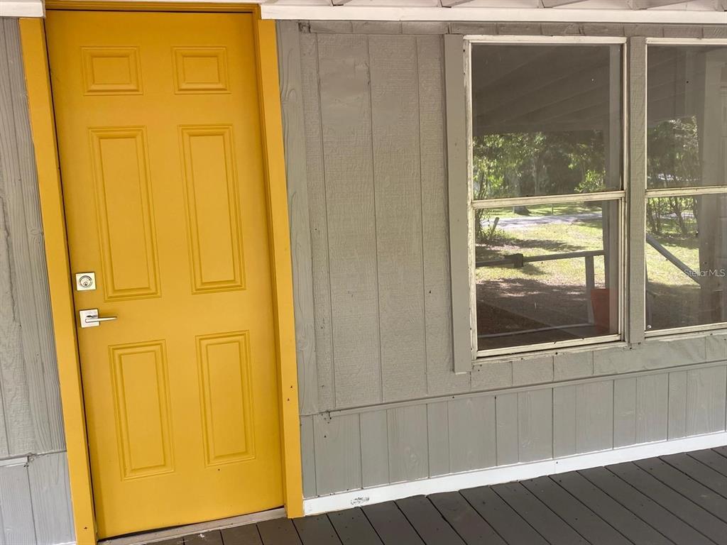 A yellow door stands next to a window on a covered porch with gray siding — 19429 MCCLOY CIRCLE, BROOKSVILLE, FL