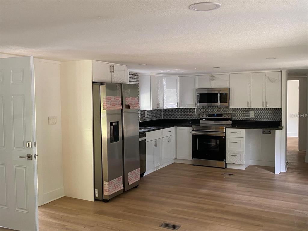 A kitchen with white cabinets, stainless steel appliances, and dark countertops over wood-look flooring — 19429 MCCLOY CIRCLE, BROOKSVILLE, FL