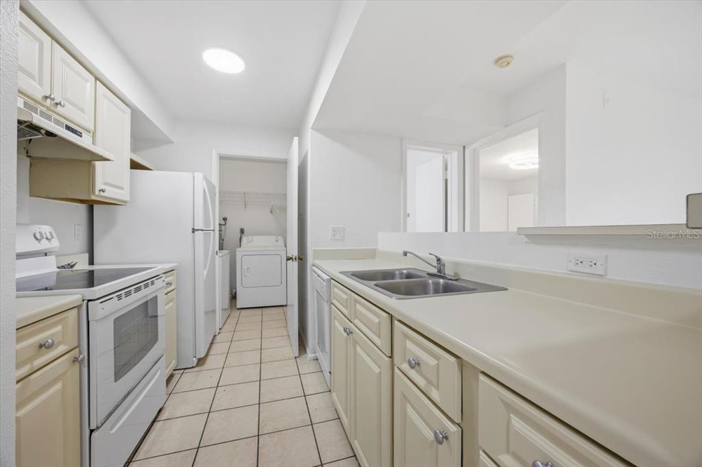 A kitchen features white cabinets, light countertops, tile flooring, and an adjacent laundry closet — 3028 PARKWAY BOULEVARD UNIT 301, KISSIMMEE, FL
