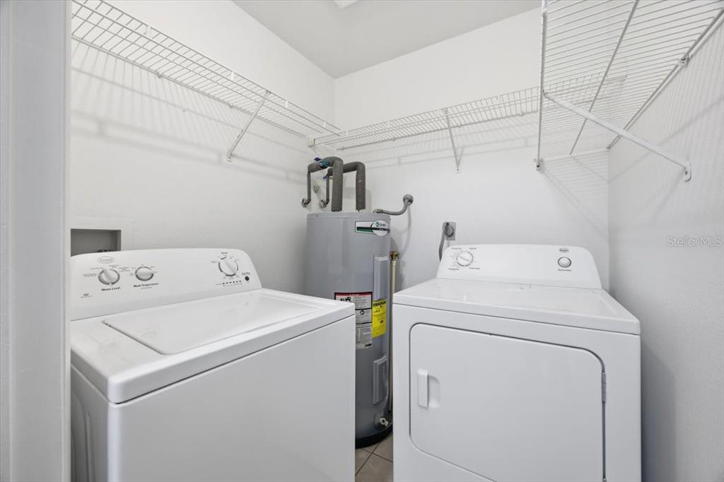 A laundry room features a white washer and dryer next to a water heater — 3028 PARKWAY BOULEVARD UNIT 301, KISSIMMEE, FL