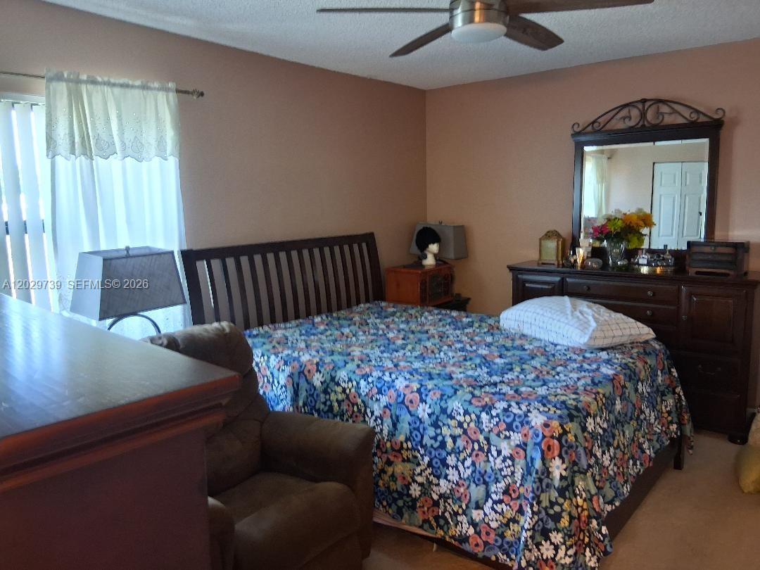 A bedroom features a bed with a floral quilt, a dresser with a mirror, and furniture — SUNRISE, FL