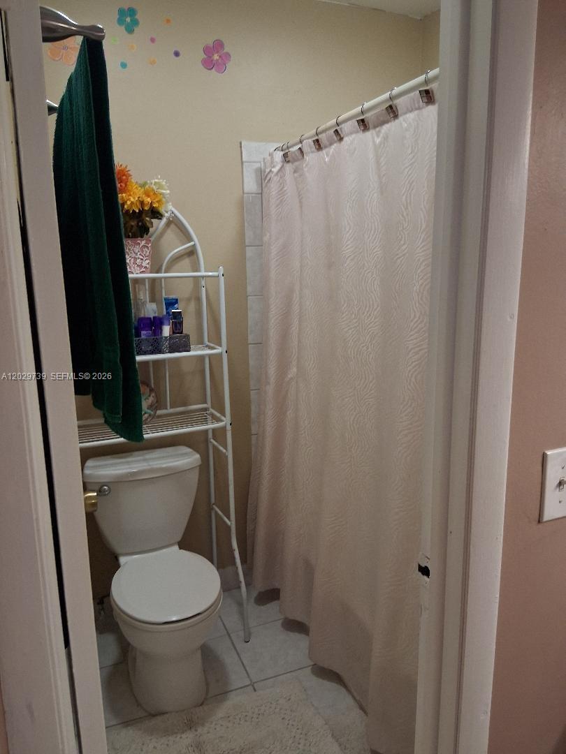 A bathroom features a white toilet, a metal storage rack, and a shower with curtains — SUNRISE, FL