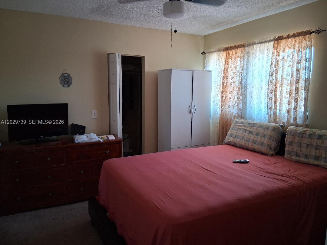 A bedroom features a bed with a red comforter, a dresser with a television, and curtains — SUNRISE, FL