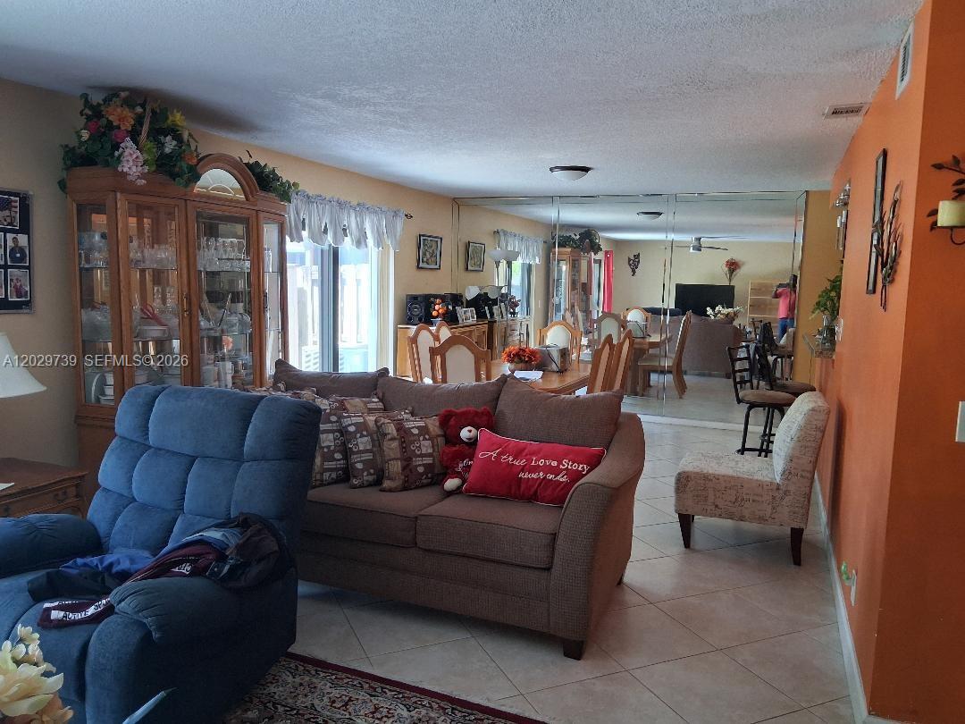 A living room features a brown sofa, a blue recliner, and a mirrored dining area wall — SUNRISE, FL