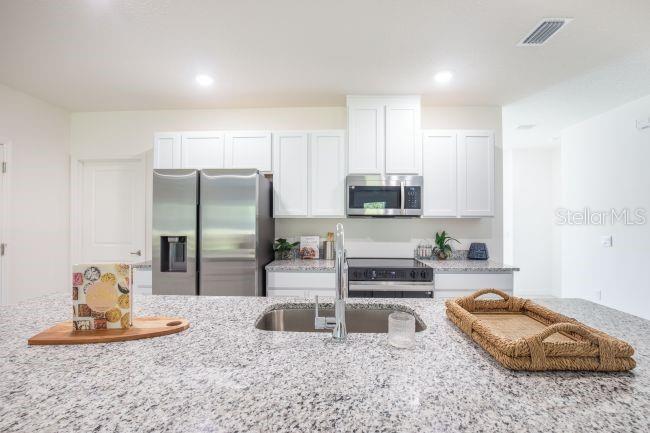 A modern kitchen features white cabinetry, stainless steel appliances, and a granite-topped island with sink — TBD LIME TREE DRIVE, EDGEWATER, FL