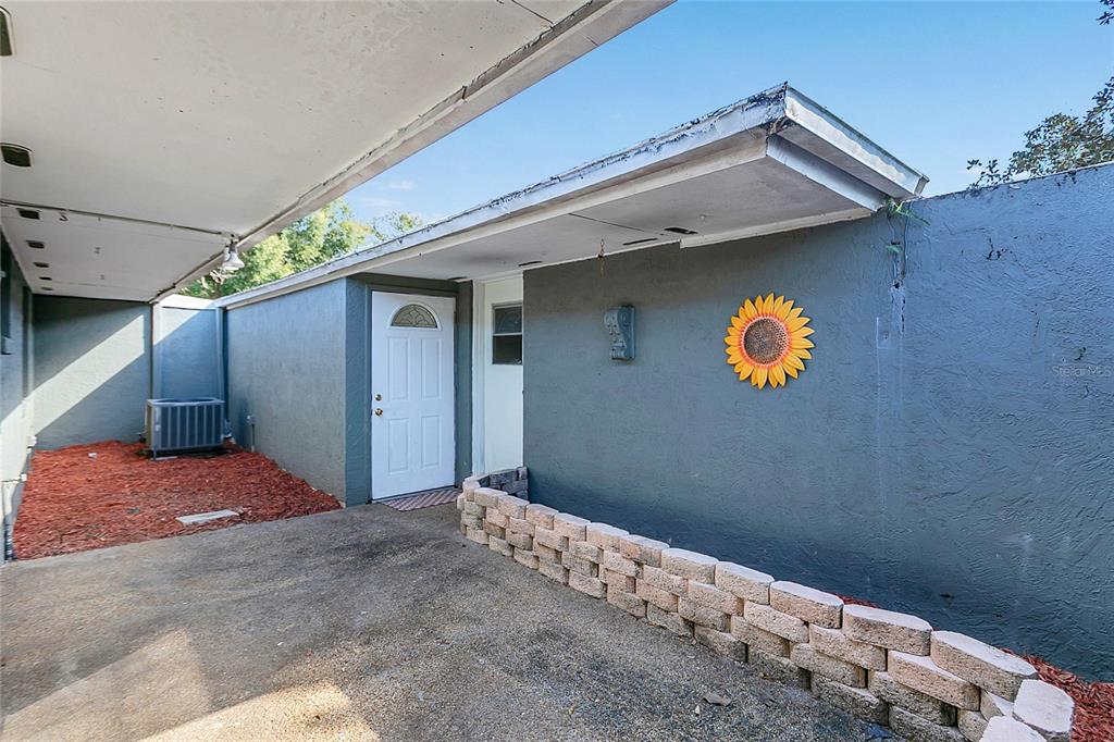 A gray exterior wall features a white door, a sunflower decoration, and a low stone planter — 561 E ORANGE STREET, ALTAMONTE SPRINGS, FL