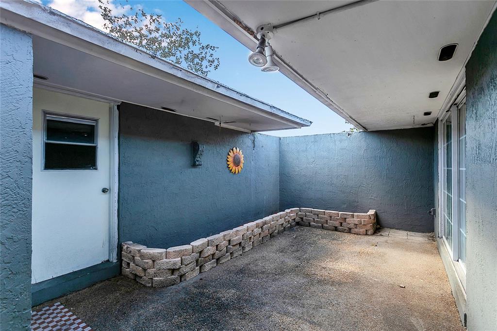 A small, enclosed concrete patio features a low stone retaining wall and a sunflower decoration — 561 E ORANGE STREET, ALTAMONTE SPRINGS, FL