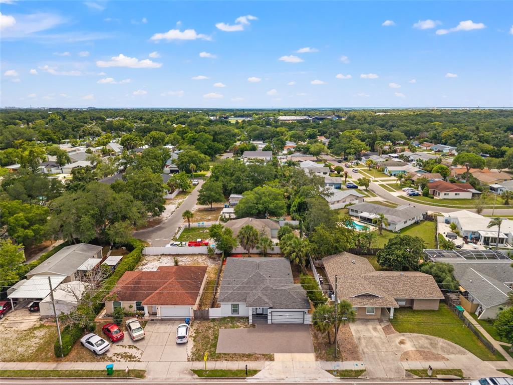 An aerial view shows three suburban houses with driveways and lawns in a residential neighborhood — 3040 BELCHER ROAD, DUNEDIN, FL