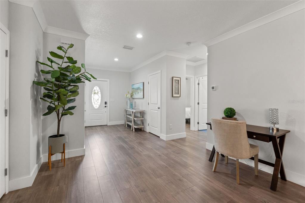 A bright entryway features wood-look flooring, a potted plant, a console table, and a desk — 3040 BELCHER ROAD, DUNEDIN, FL
