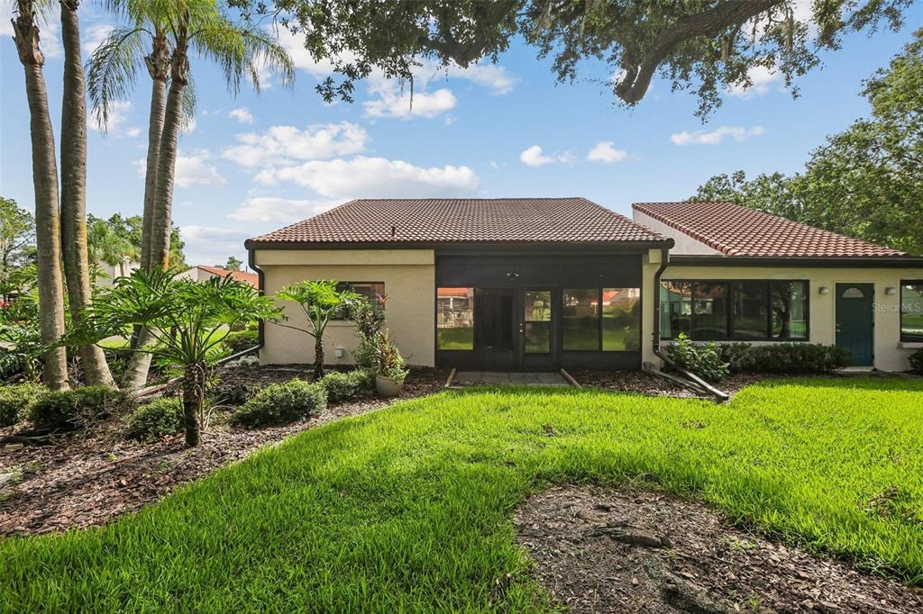 The rear exterior of a house features a screened-in patio, tile roof, and grassy lawn — 107 SEVILLE COURT N, PLANT CITY, FL