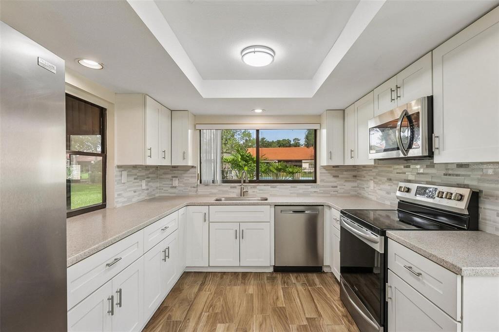 A kitchen features white cabinets, stainless steel appliances, a tiled backsplash, and wood-look flooring — 107 SEVILLE COURT N, PLANT CITY, FL