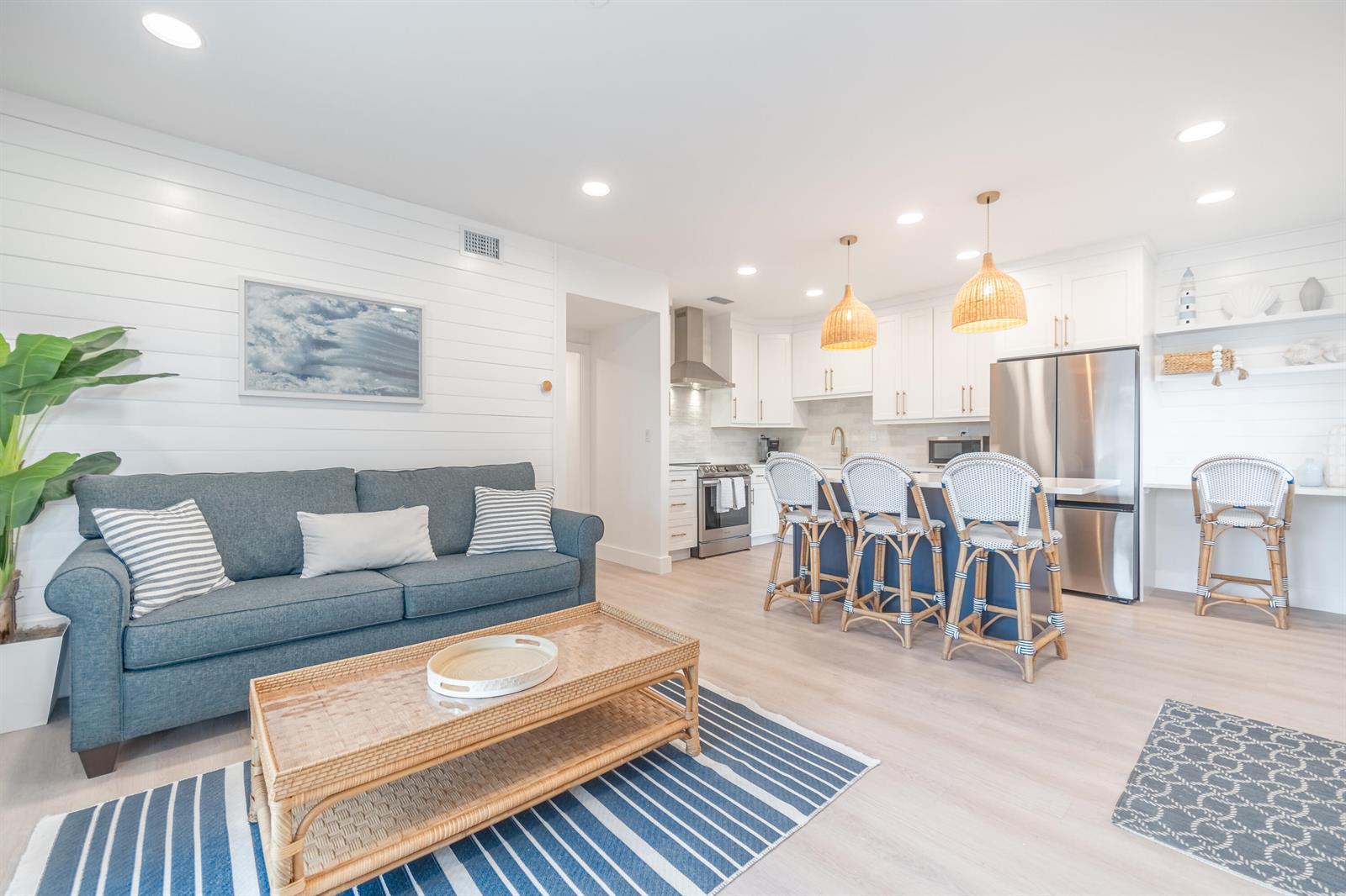 A living room with a blue sofa and a kitchen featuring white cabinets and stools — 353 S Us Highway 1 # A6, Jupiter FL 33477, JUPITER, FL