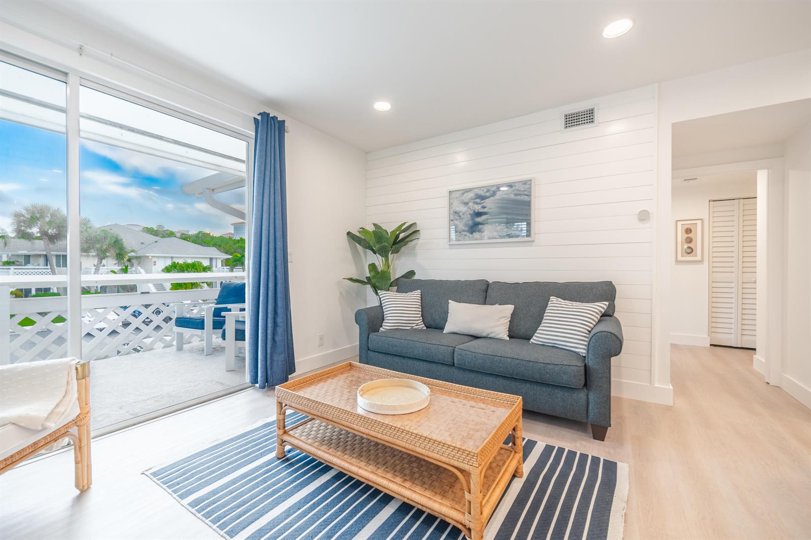 A living room features a blue sofa, a wicker coffee table, and a balcony view — 353 S Us Highway 1 # A6, Jupiter FL 33477, JUPITER, FL