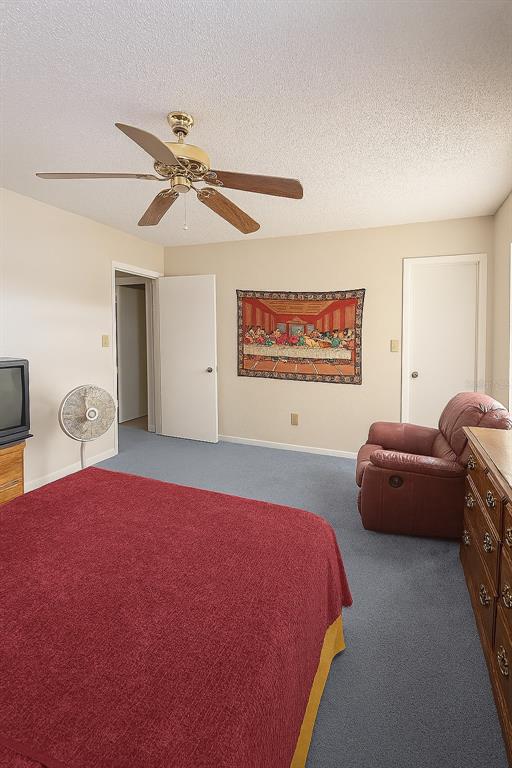 A bedroom features a red bedspread, a recliner, a ceiling fan, and a wall tapestry — 2417 NE 6TH STREET UNIT 8, OCALA, FL