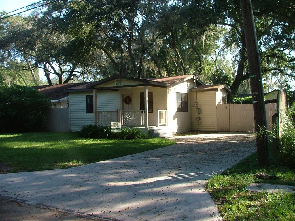 A single-story house with light siding and a front porch sits behind a concrete driveway — 11709 HOYT AVENUE, TAMPA, FL