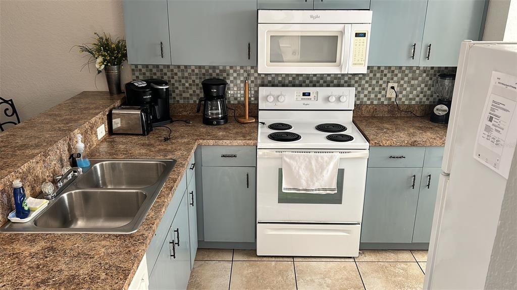 A kitchen features blue cabinets, brown laminate countertops, white appliances, and a tiled backsplash — 9202 LAKE MARION GOLF RESORT UNIT A, KISSIMMEE, FL