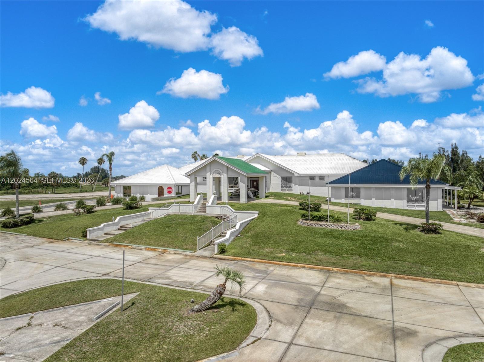 A large white building with a green roof and a paved driveway under blue skies — 6813 Heavitree, Sebring FL 33876, SEBRING, FL