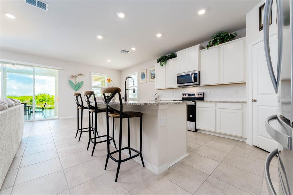 A kitchen features white cabinets, granite countertops, a center island with bar stools, and tile flooring — 3719 LIVELY CORAL PLACE, BRADENTON, FL